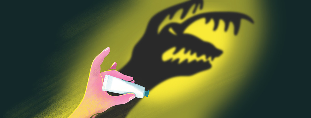 A hand holding a pill is casting a shadow of a scary monster.