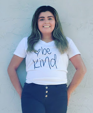 Daisy smiles as she poses in a shirt that says "be kind"