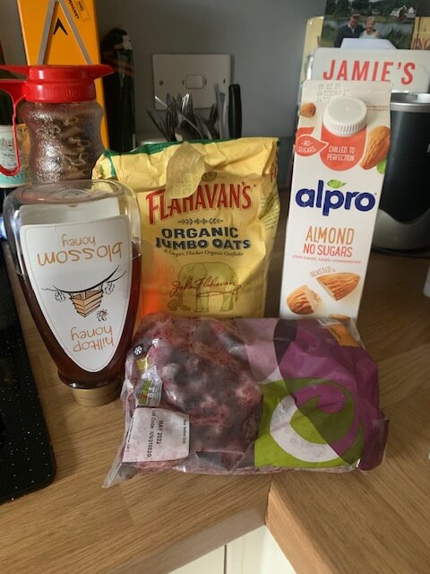 Ingredients for a smoothie including oats, honey, almond milk, and frozen blueberries.