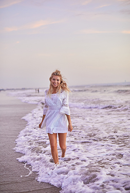  Camille Knowles smiling and walking through waves crashing on the beach.