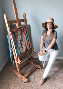 Photo of a woman in front of a painting sitting on an easel